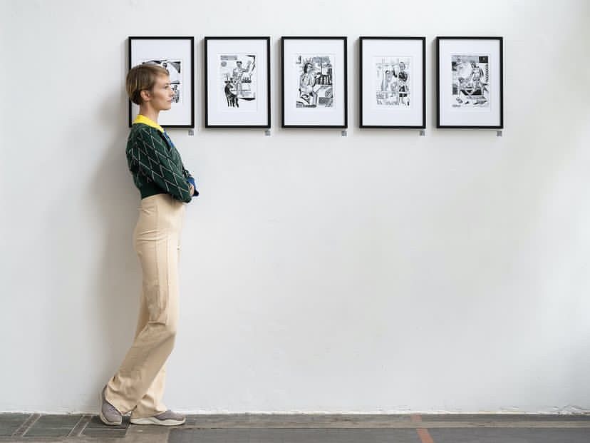 “200 Revelations” exhibition by Sylwia Zawiślak at Raster Gallery, Warsaw, 2022. Linocut prints depicting symbolic figures are displayed on the walls. Visitors are viewing the artworks.